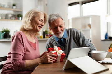 Obraz na płótnie Canvas Senior couple having video call. Happy husband giving his wife a gift.