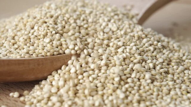 Pouring raw quinoa seeds into a wooden spoon in slow motion. Macro shot. Super food concept