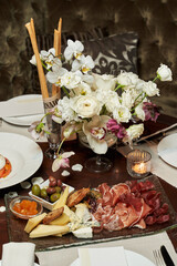 meat and cheese delicacies on a table decorated with a bouquet of white flowers