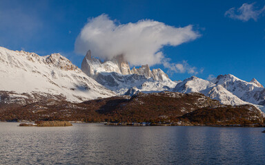 Panorama image of  a mountain range with the summit of the Cerro Fitzroy shrouded in clouds with the lake 'Laguna Capri' in the foreground
