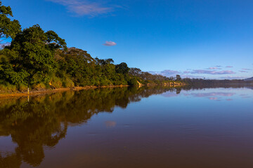 Fototapeta na wymiar Late afternoon sunlight adds a glow to the river bank foliage and reflections of trees and clouds in the still, dark waters of a large river in east coast Australia.