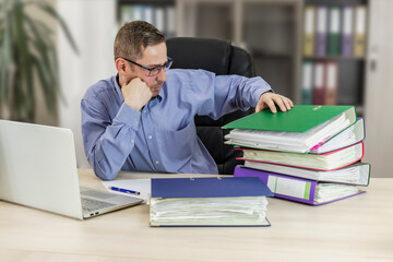 Boss businessman at his desk in the office with a bunch of folders with papers. Strenuous office...