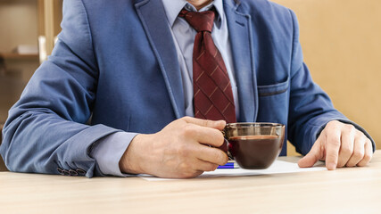 A man in a business suit holds a cup of hot coffee in his hands. Morning businessman. Close-up.