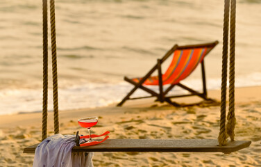 Fototapeta na wymiar a glass of cocktail and sunglasses on swing with blurred empty beach chair background on the calm beach