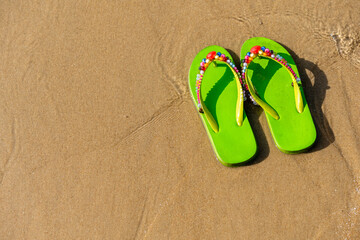 Fototapeta na wymiar Green decorated flip flops on the beach