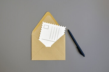 Open envelope made of craft paper, empty postcard and blue ballpoint pen on gray background....