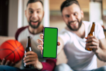 Close up mockup photo of green blank screen on the smart phone in hand of excited young bearded...