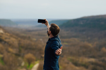 Young man with hand up taking a selfie on the mountain. Travel, lifestyle.