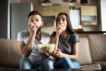 Beautiful smiling modern couple in love is watching some film or movie on TV while they relaxing on the couch at own apartment