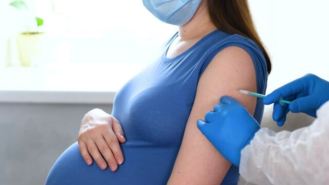 Pregnant Vaccination. Doctor giving COVID - 19 coronavirus vaccine injection to pregnant woman. Doctor Wearing Blue Gloves Vaccinating Young Pregnant Woman In Clinic. People vaccination concept.