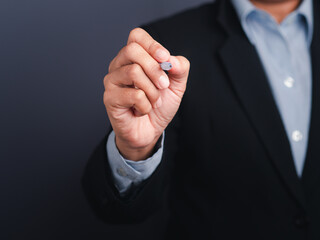 A businessman wearing a suit is holding a pen write or writing on the virtual screen or in the air against a gray background. Space for text. Close-up. Modern business background concept