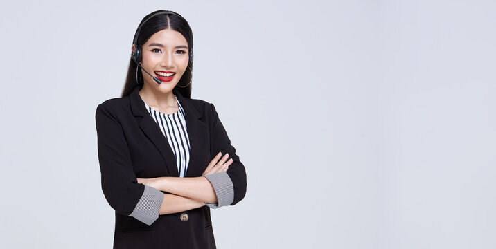 Smiling Asian businesswoman customer support phone operator isolated over gray background. call center and customer service concept.