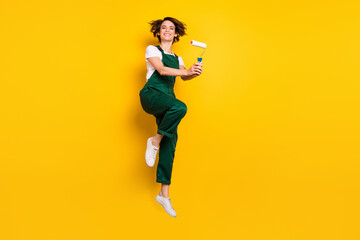 Fototapeta na wymiar Full size photo of young pretty smiling woman painter jumping with roller restoration isolated on yellow color background