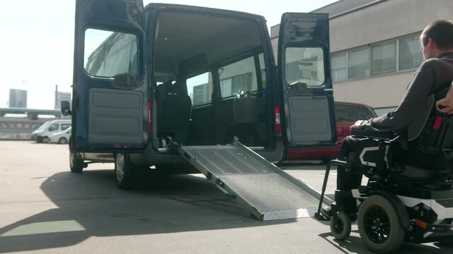 Assistant helping disabled person on wheelchair with transport using accessible vehicle ramp
