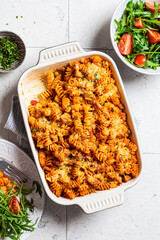 Baked pasta with chicken and cheese in oven dish with green salad, top view, gray background. Italian cuisine concept.