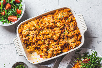 Baked pasta with chicken and cheese in oven dish with green salad, top view, gray background....