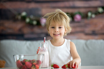 Cute toddler child, blond boy, drinking smoothie and easting strawberries