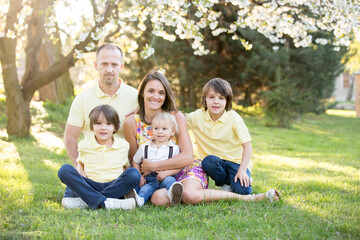 Fototapeta premium Beautiful family, mother, father and three kids, boys, having familly outdoors portrait taken on a sunny spring evening, beautiful blooming garden, sunset time