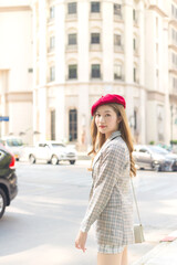 Asian beautiful woman with bronze hair wears red cap is walking across the street.