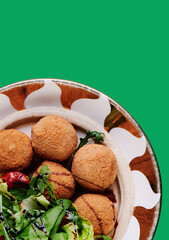 Beautiful falafel balls and fresh salad on a plate isolated on a green background. Space for text. Close-up.
