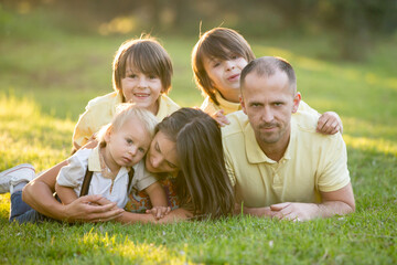 Naklejka na ściany i meble Beautiful family, mother, father and three kids, boys, having familly outdoors portrait taken on a sunny spring evening, beautiful blooming garden, sunset time