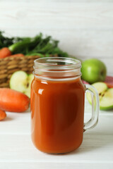 Jar of apple - carrot juice and ingredients on white wooden background