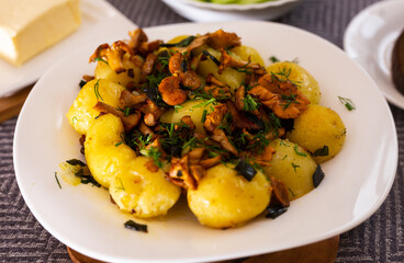 baked  potatoes with chanterelles, served with herbs on white plate