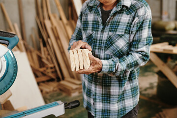 Cropped image of senior carpenter holding freshly cut wooden blocks he prepared for furniture item