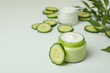 Jars with cosmetic cream, cucumber slices and branch on white table