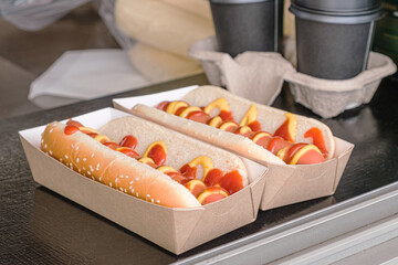 Two hot dogs in a cardboard box and two cardboard cups of coffee on the counter of a street food...