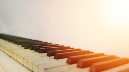 old piano keyboard in sunbeams of orange hue light, black and white piano keys and there is a place for an inscription, white ancient piano