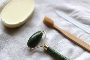 Jade face roller, wooden toothbrush, glass nail file and bar of soap. Sustainable body care products. Selective focus.