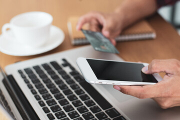 Businesswoman hand holding on smart phone and credit card on office deck to pay for items through an online payment system. Online shopping is the best option to reduce the spread of the coronavirus.