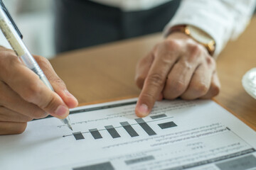 Businessman wearing white shirt analyzing income charts and graphs with hand holding pen on office desk. Close up.Business analysis and strategy concept.