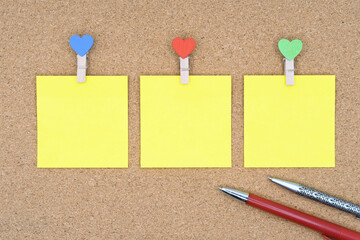 Three yellow stickers with multi-colored clothespins and ballpoint pens on a cork board.