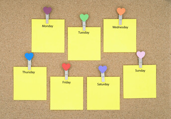 Seven yellow sticky notes with days of the week on a cork board.
