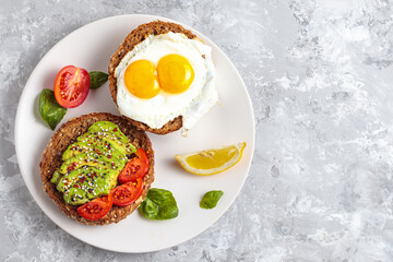 Avocado toast breakfast with fried egg, top view. Fresh avocado burger, vegetarian snack, delicious dark bread, natural avocado slices on plate. Gourmet diet appetizer