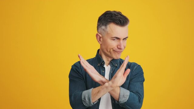 A disgruntled man showing no gesture with crossing arms while standing in the yellow studio