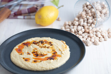 Home made hummus bowl, decorated with boiled chickpeas, lemon and olive oil over a rustic white background.