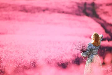 Zelfklevend Fotobehang meisje in een veld met lila bloemen in lavendelkleuren, violet en roze landschap, gelukkig en harmonie © kichigin19