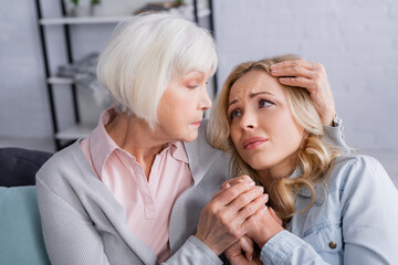 Elderly mother hugging displeased daughter at home