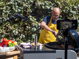 CAUCASIAN MAN IN YELLOW APRON. BARBECUING ON LINE. COOKING COURSE. COOKING IN STREAMING