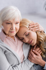 Senior woman embracing and holding hand of adult daughter