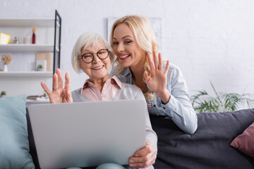 Smiling daughter and mother having video call on laptop