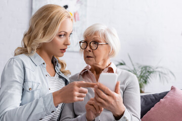 Woman talking to senior mother with smartphone on blurred foreground