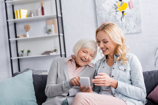 Cheerful women using smartphone on couch in living room