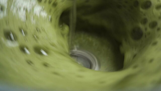 Frothing foam of green matcha tea in slow motion close-up. Electric whisk foamer. Macro shot