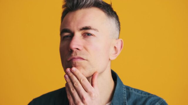 A portrait of a smiling mature man touching his shaving face in the yellow studio