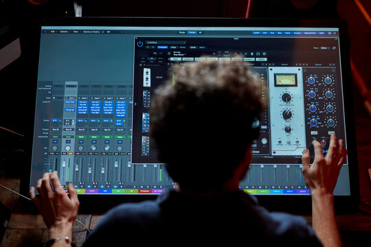 Man working in music studio using large computer screen shot from behind