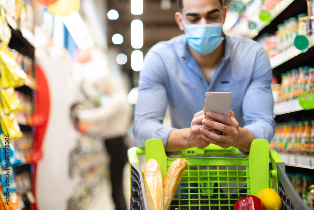 Wall mural Arabic Man Doing Grocery Shopping Using Smartphone In Supermarket